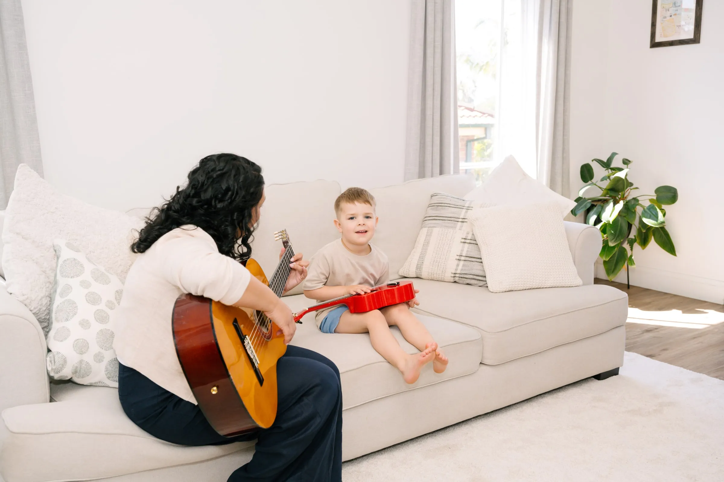 Maria playing guitar while a boy strums a red ukulele