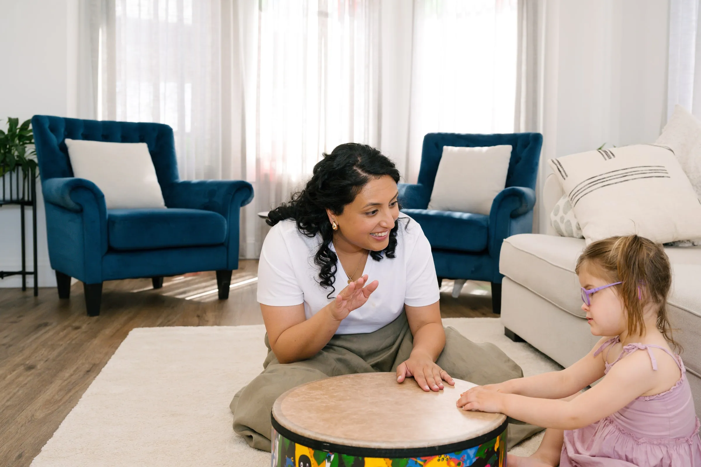 Maria and a young girl playing a large drum together at home
