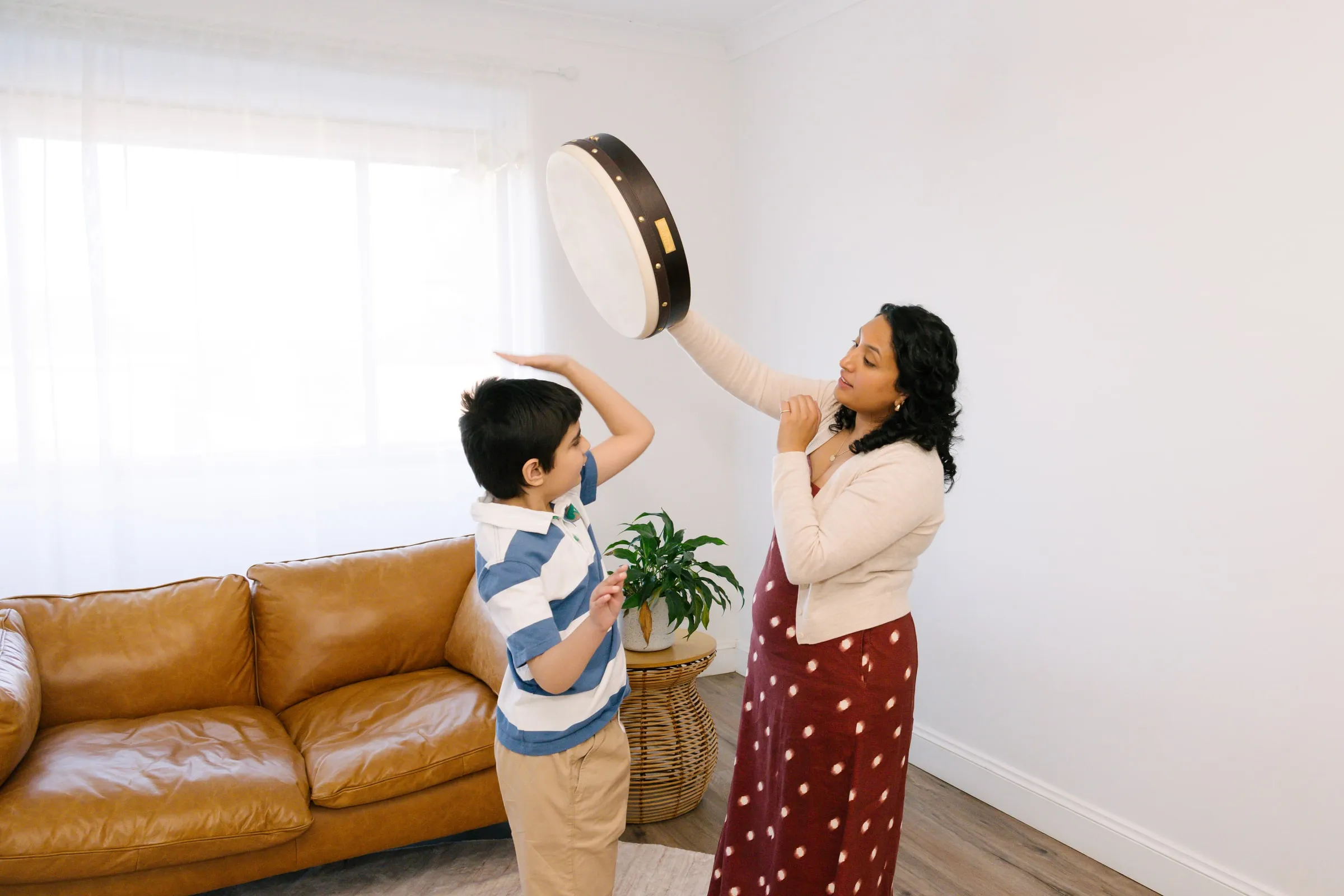 Maria and a boy reaching up to tap a frame drum