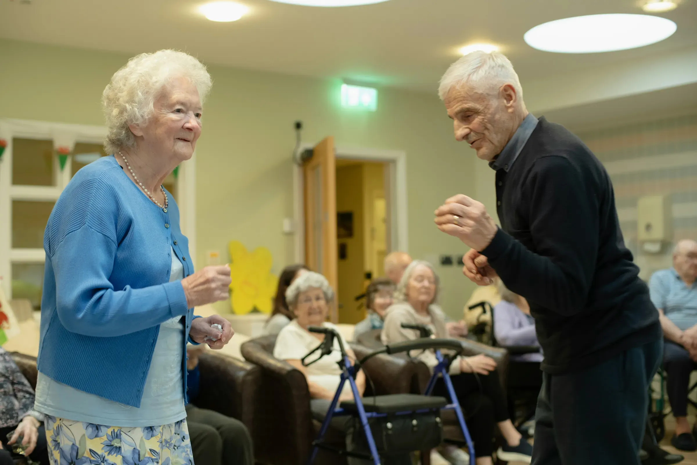 An older woman and man smiling and dancing together during a music session in an aged care home