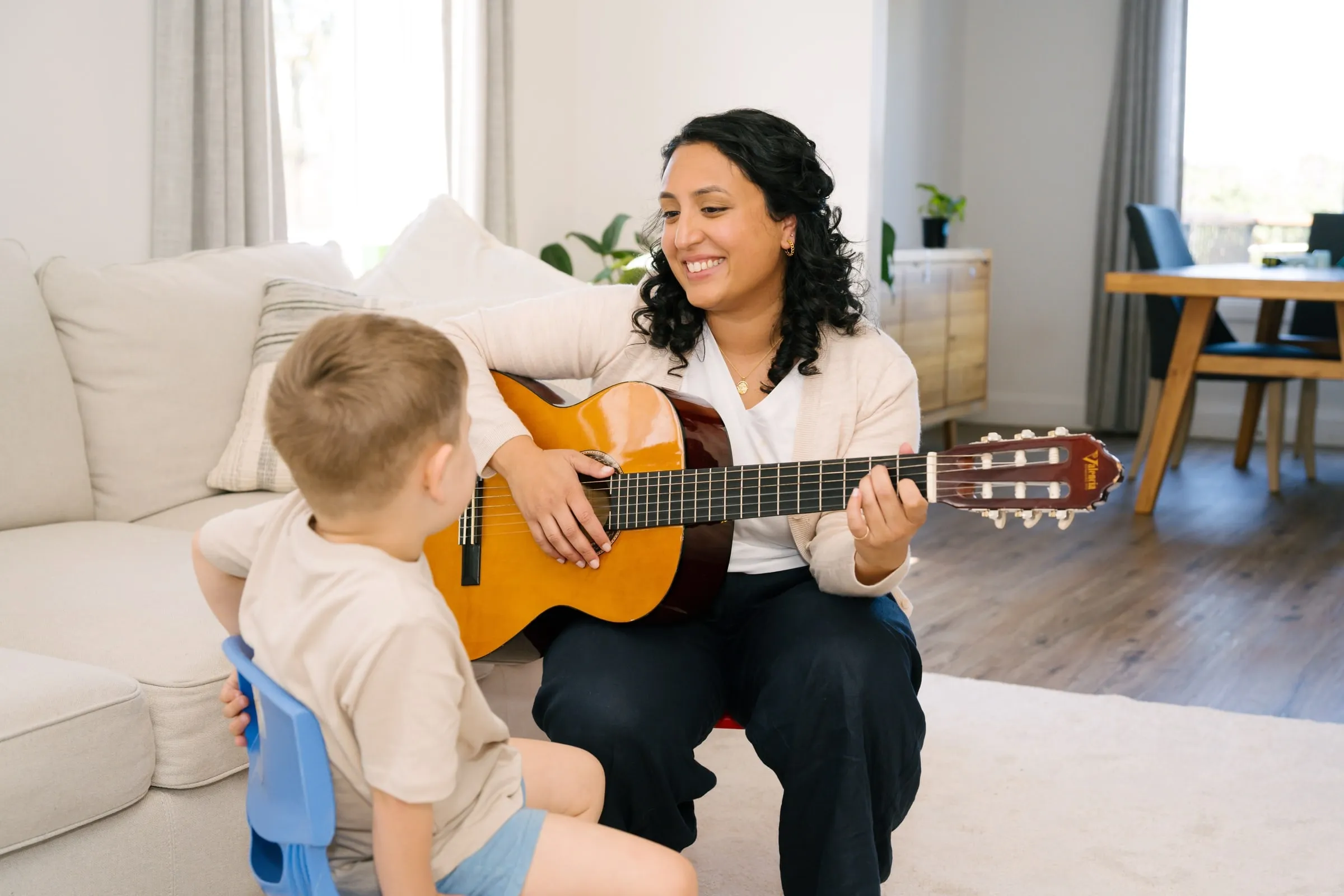 Maria playing guitar to a young boy on the sofa in his home
