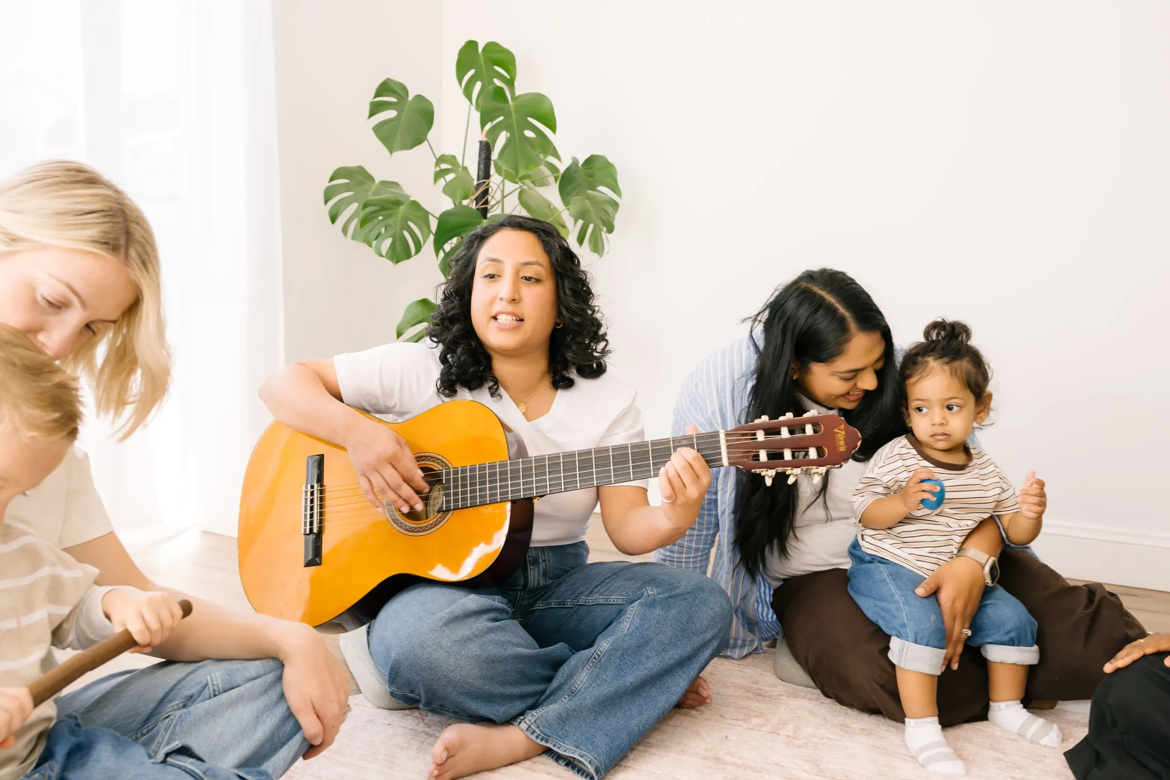 Toddlers and their parents in a circle while Maria plays guitar